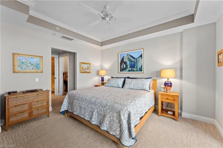 Carpeted bedroom with ornamental molding, connected bathroom, ceiling fan, and a tray ceiling
