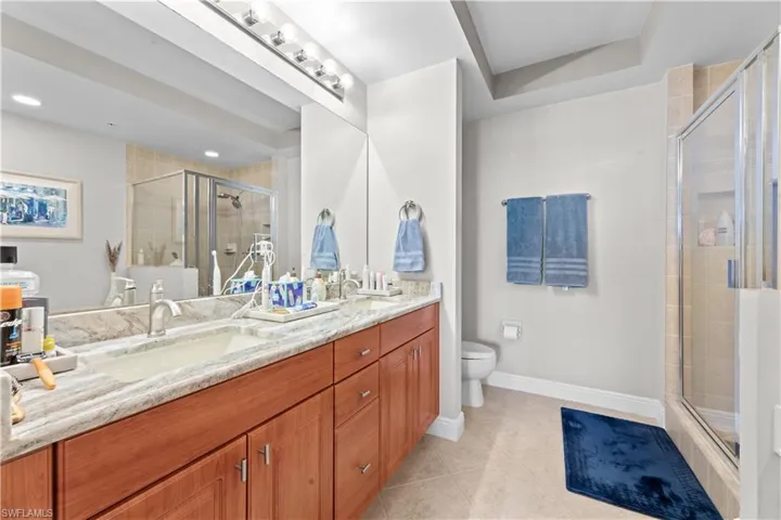Bathroom with a shower with door, tile patterned floors, toilet, and double sink vanity