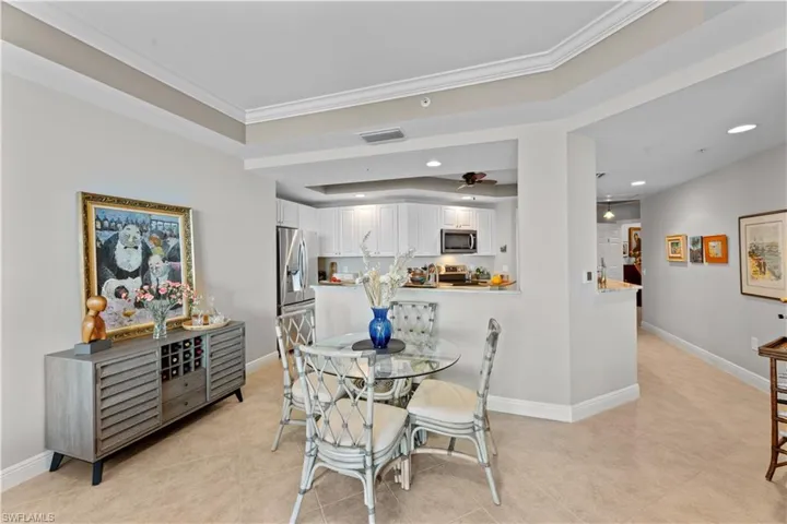 Dining room featuring light tile patterned floors, ceiling fan, a raised ceiling, and crown molding