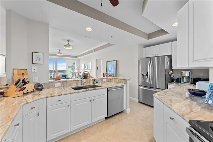 Kitchen with stainless steel appliances, sink, white cabinetry, ceiling fan, and a raised ceiling