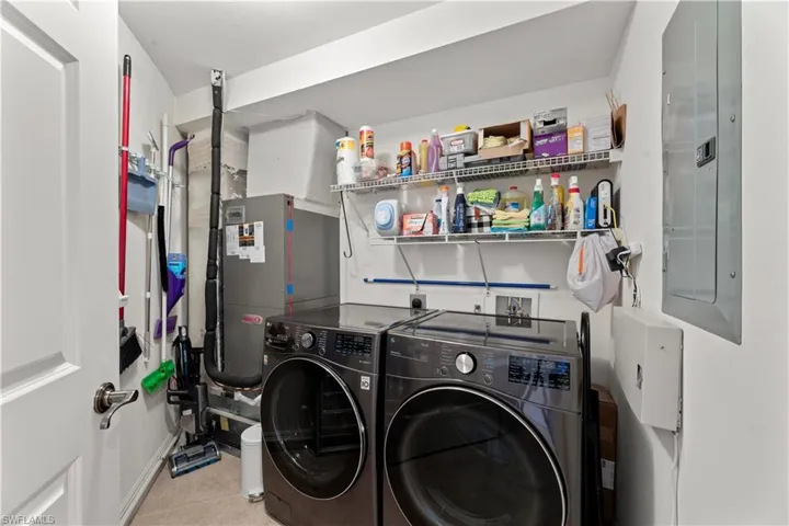 Washroom with electric panel, light tile patterned floors, and washing machine and clothes dryer