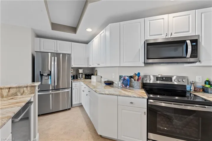 Kitchen featuring light tile patterned flooring, appliances with stainless steel finishes, light stone countertops, and white cabinets