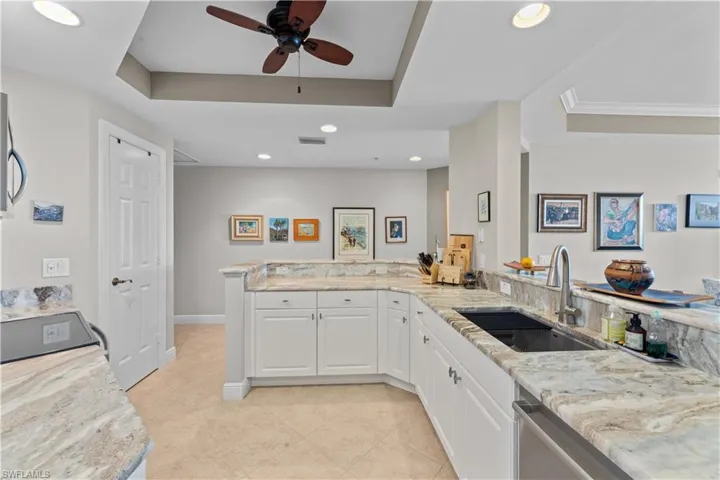 Kitchen featuring ceiling fan, sink, light tile patterned floors, and a tray ceiling
