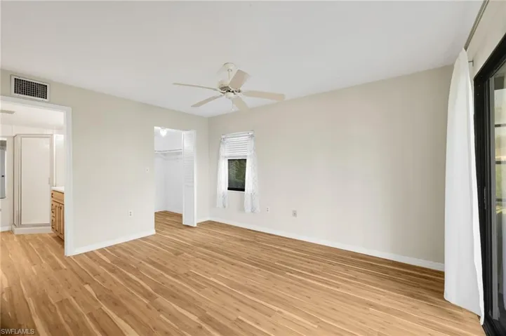 Unfurnished bedroom featuring light wood-type flooring, a spacious closet, a ceiling fan, and ensuite bathroom