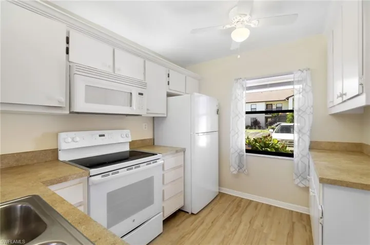 Kitchen with white appliances, light countertops, light wood-style flooring, white cabinets, and ceiling fan