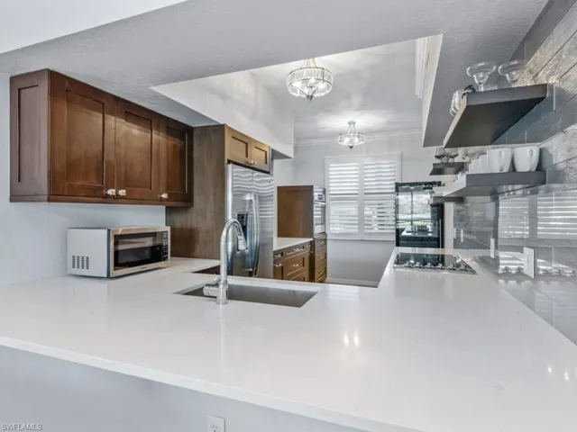 Kitchen with open shelves, light countertops, appliances with stainless steel finishes, a peninsula, and a sink
