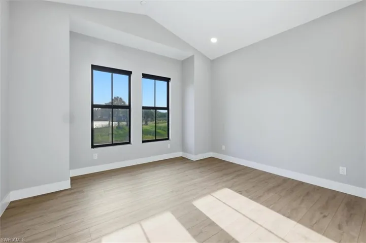 Bright corner bedroom featuring dual black-framed windows with expansive natural light, wood-finish flooring, and clean white walls with recessed ceiling lighting