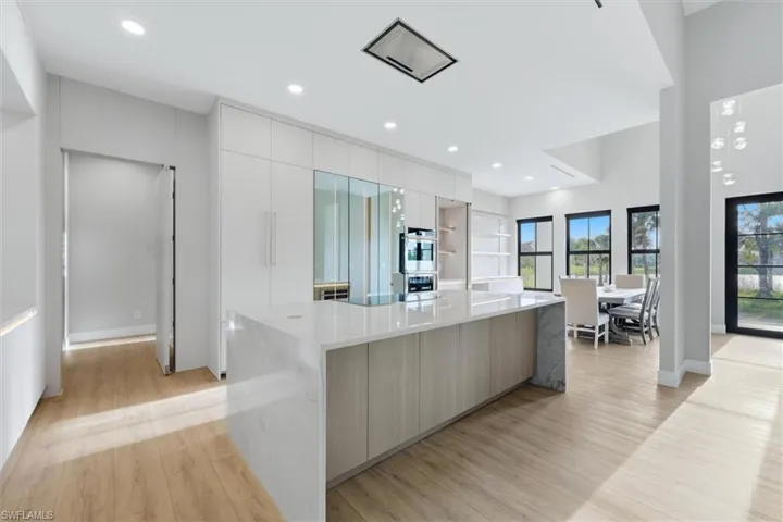 Expansive kitchen island with a light-toned countertop, integrated oven and microwave, recessed lighting, and wood-finish flooring