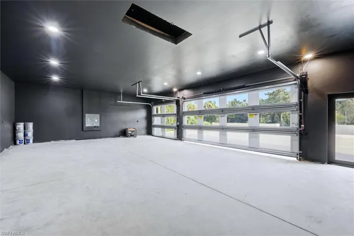 Spacious garage featuring polished concrete flooring, modern recessed and pendant lighting, glass overhead door with natural light, and black finished walls with contemporary hardware and storage infrastructure