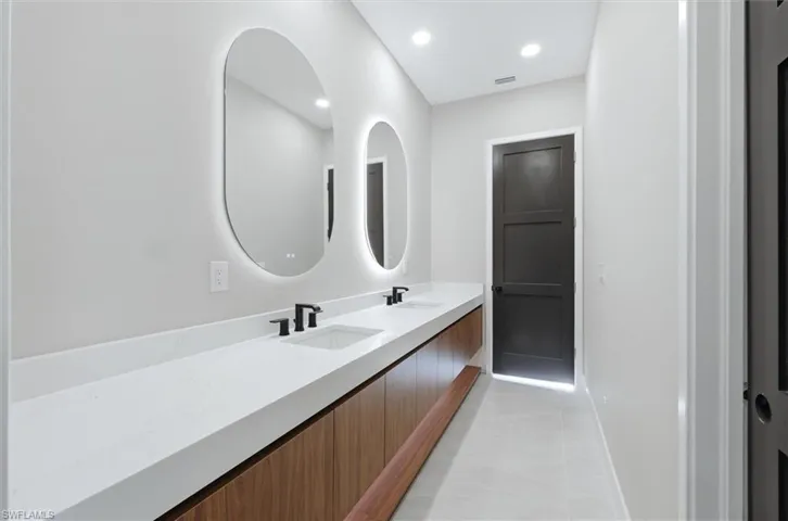 Double vanity with undermount sinks, illuminated oval mirrors, wood-finish cabinetry, and matte black fixtures