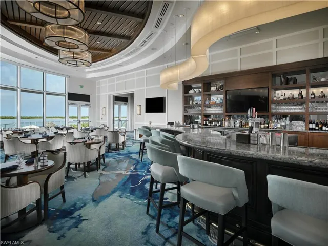 Curved stone-topped bar with built-in cabinetry, coffered ceiling with circular light fixtures, wave-patterned ribbon lighting, and floor-to-ceiling windows