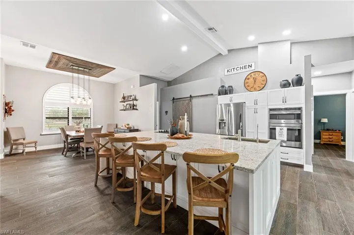Kitchen featuring a breakfast bar area, appliances with stainless steel finishes, a barn door, light stone countertops, and white cabinets