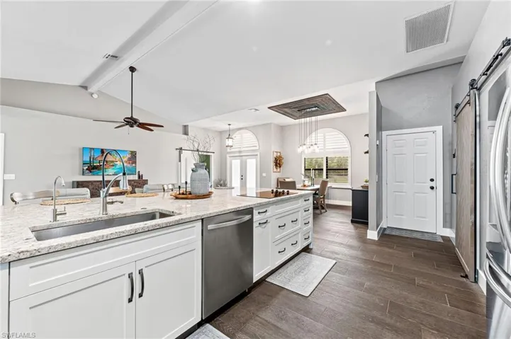 Kitchen featuring sink, white cabinetry, stainless steel appliances, light stone countertops, and a barn door