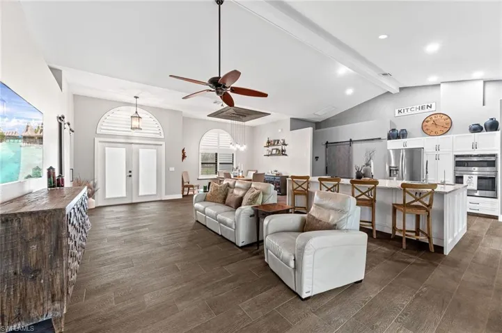 Living room featuring vaulted ceiling with beams, a barn door, ceiling fan, and french doors