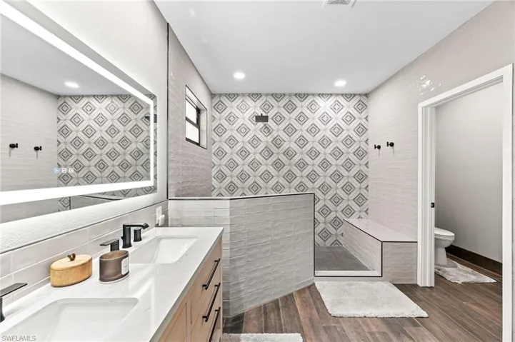 Bathroom with toilet, a shower, wood-type flooring, tile walls, and vanity