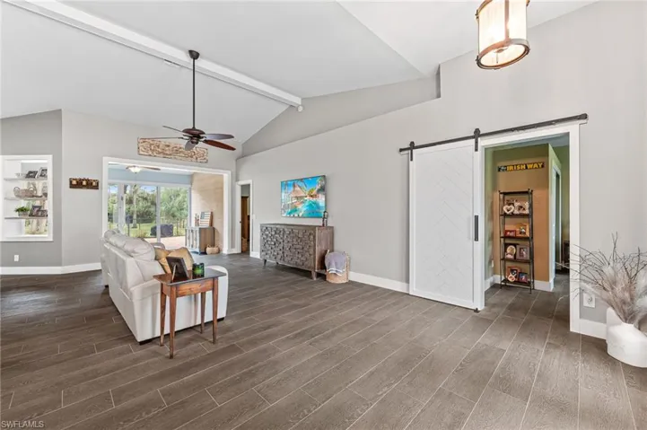 Living room featuring a barn door, dark hardwood / wood-style floors, vaulted ceiling with beams, and ceiling fan