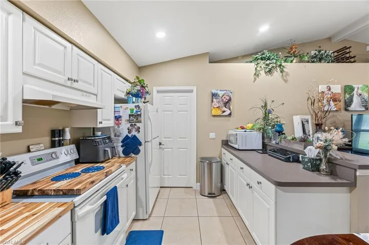 Kitchen featuring white cabinetry, white appliances, light tile patterned floors, and vaulted ceiling with beams