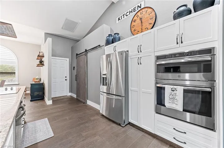 Kitchen featuring lofted ceiling, stainless steel appliances, a barn door, and white cabinets