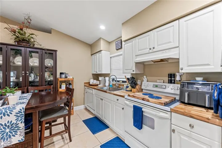 Kitchen featuring sink, white appliances, butcher block counters, white cabinets, and light tile patterned flooring