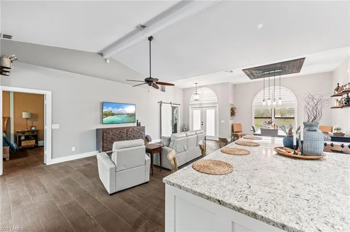 Living room featuring vaulted ceiling with beams, ceiling fan with notable chandelier, and french doors