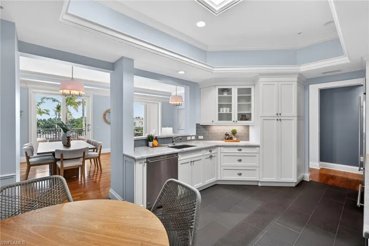 Kitchen featuring a raised ceiling, glass insert cabinets, dark tile patterned floors, stainless steel dishwasher, and light stone counters