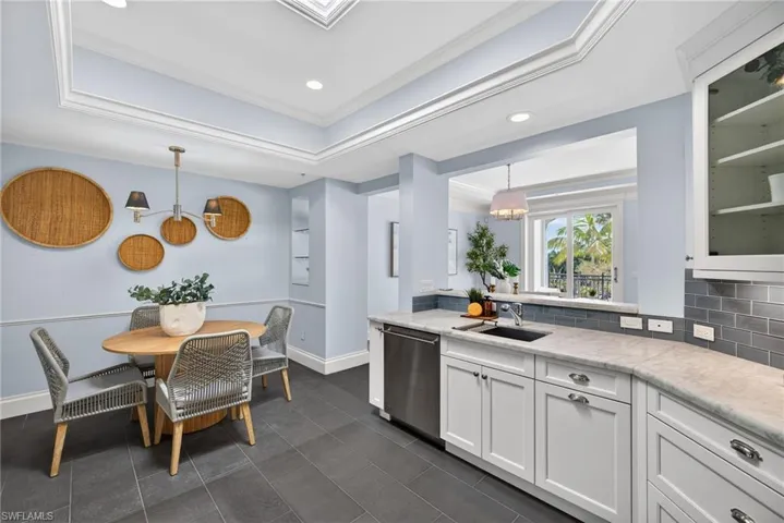 Kitchen with a raised ceiling, backsplash, glass insert cabinets, white cabinets, and hanging light fixtures