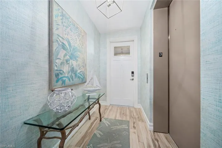 Hall with elevator, an inviting chandelier, and light wood-type flooring
