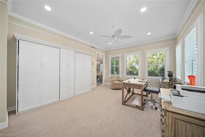 Carpeted home office with ceiling fan and crown molding