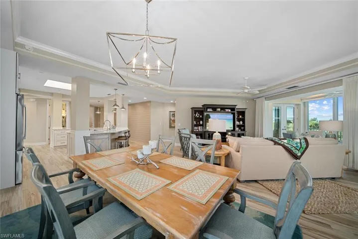 Dining space with a skylight, light wood-type flooring, a tray ceiling, ceiling fan with notable chandelier, and ornamental molding