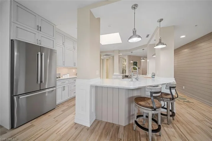Kitchen with a skylight, light stone counters, light hardwood / wood-style flooring, stainless steel fridge, and pendant lighting