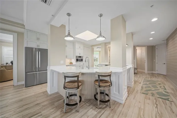 Kitchen featuring decorative light fixtures, light hardwood / wood-style flooring, a large island, white cabinetry, and stainless steel appliances