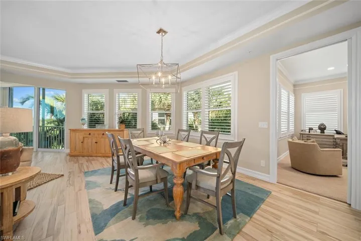 Dining area featuring a raised ceiling, a chandelier, light hardwood / wood-style floors, and ornamental molding