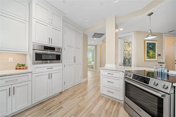 Kitchen with white cabinetry, stainless steel appliances, light hardwood / wood-style flooring, backsplash, and pendant lighting