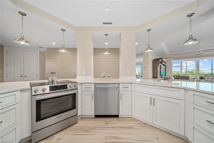 Kitchen featuring light stone counters, light hardwood / wood-style flooring, pendant lighting, white cabinets, and appliances with stainless steel finishes
