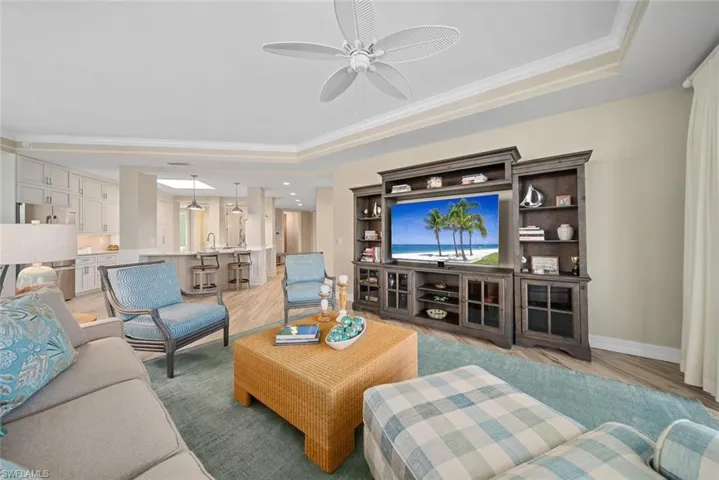 Living room featuring ceiling fan, light wood-type flooring, crown molding, and a tray ceiling