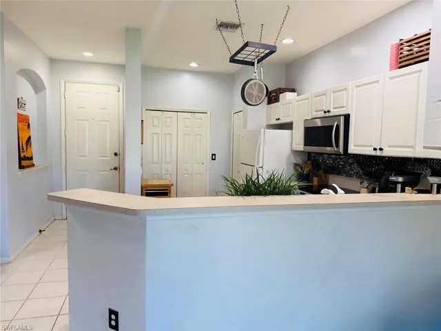 Kitchen featuring white cabinetry, stainless steel microwave, light countertops, tasteful backsplash, and light tile patterned flooring