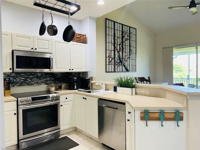 Kitchen with a peninsula, stainless steel appliances, light countertops, backsplash, and light tile patterned floors