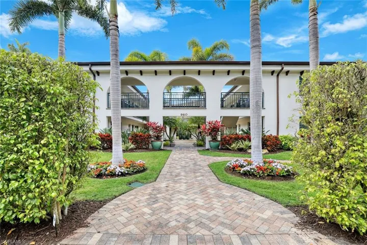 Charming Old Naples courtyard entrance framed by lush landscaping and tropical palms.
