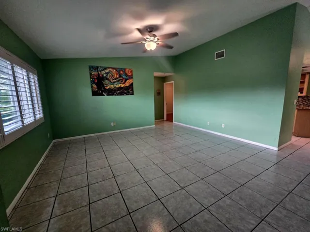 Tiled empty room with ceiling fan and lofted ceiling