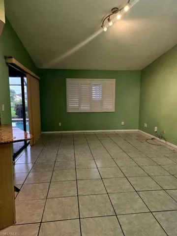 Tiled empty room featuring lofted ceiling and track lighting