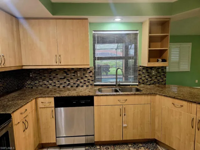 Kitchen with stone counters, sink, stainless steel dishwasher, and tasteful backsplash