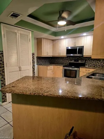 Kitchen with appliances with stainless steel finishes, tasteful backsplash, light brown cabinets, dark stone countertops, and ceiling fan