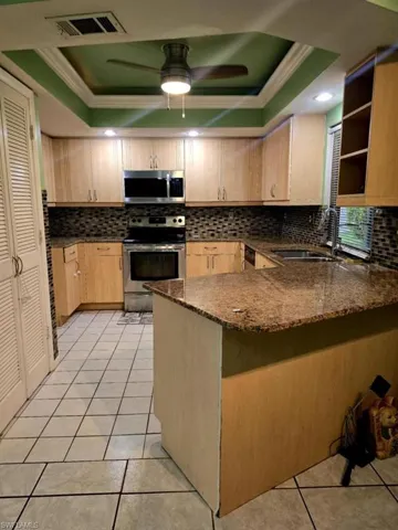 Kitchen featuring decorative backsplash, a raised ceiling, appliances with stainless steel finishes, and sink