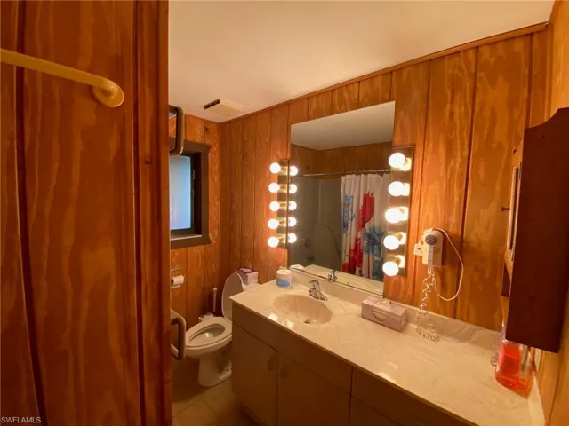 Bathroom featuring vanity, wood walls, tile patterned flooring, a shower with curtain, and toilet