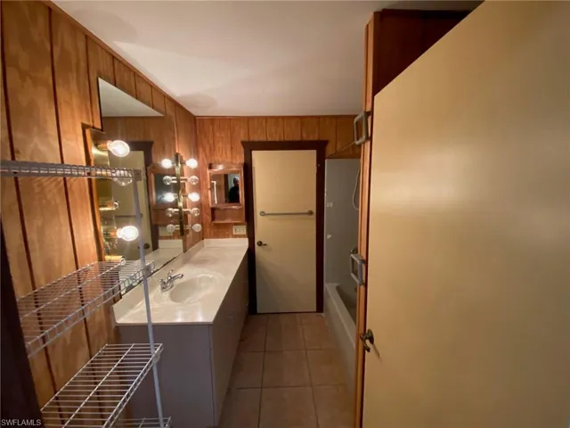 Bathroom featuring  shower combination, vanity, wood walls, and tile patterned flooring