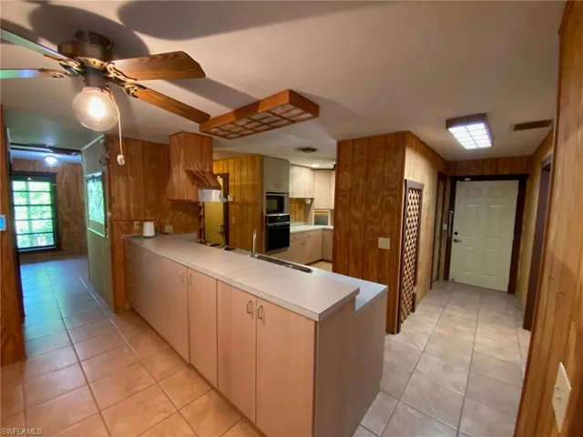 Kitchen featuring light tile patterned flooring, kitchen peninsula, black oven, and wooden walls