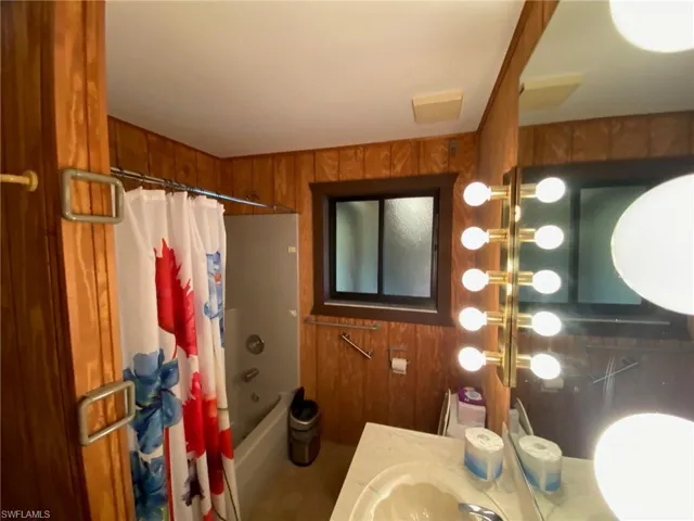Bathroom featuring shower / bath combination with curtain, wood walls, and vanity