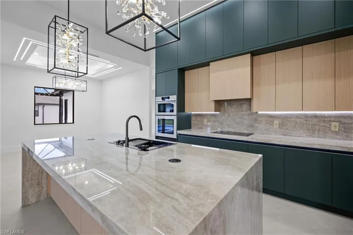 Kitchen with decorative backsplash, light tile patterned flooring, light stone countertops, an island with sink, and decorative light fixtures