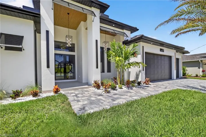 View of exterior entry with an attached garage, stucco siding, and decorative driveway