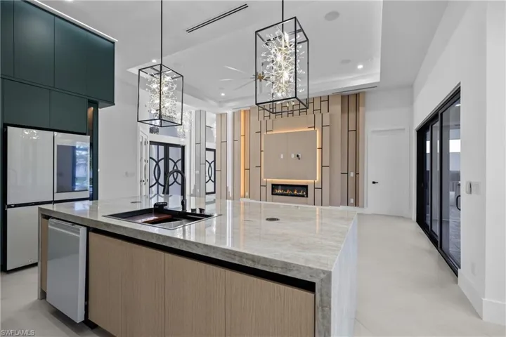 Kitchen with a kitchen island with sink, white appliances, a glass covered fireplace, modern cabinets, and a tray ceiling